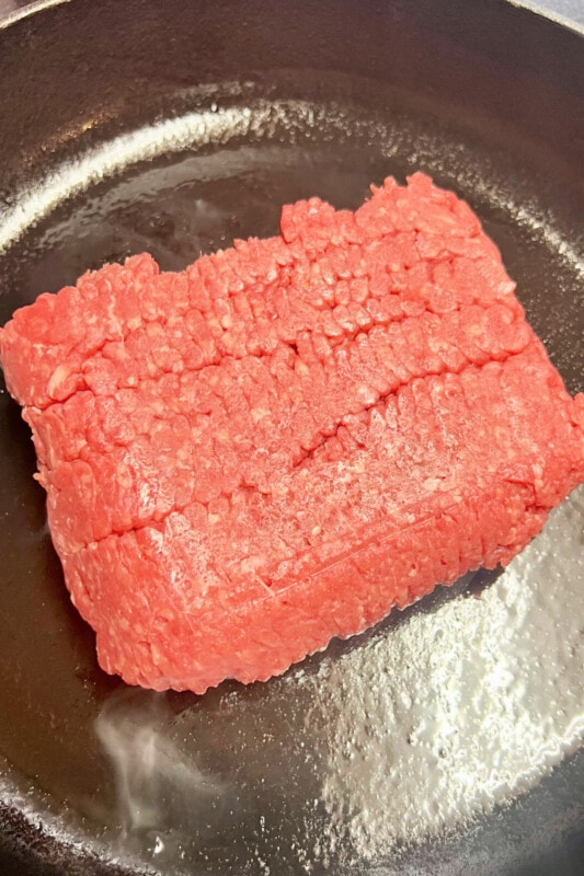 A chunk of ground beef placed into a preheated skillet to cook.