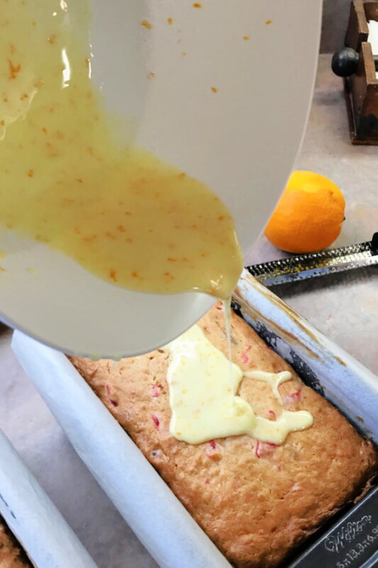 Rum glaze being drizzled over the top of a warm loaf of banana bread.