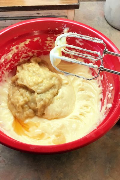 Banana bread batter with mashed bananas in a red mixing bowl.