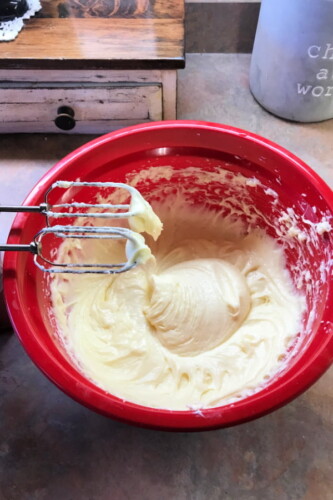 Banana bread batter in a red mixing bowl with beaters on the side.
