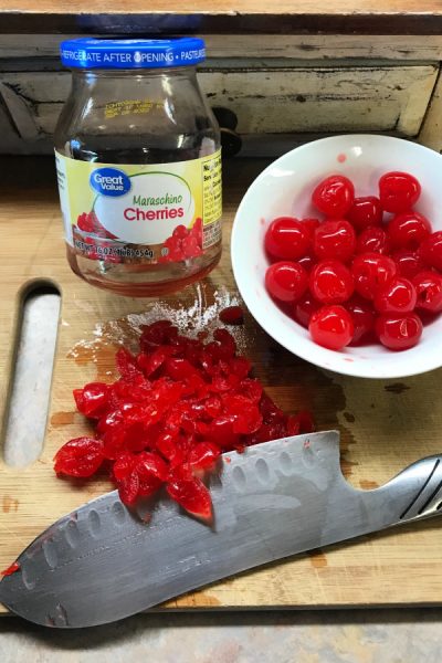 Maraschino cherries in bowl and on cutting board with knife.