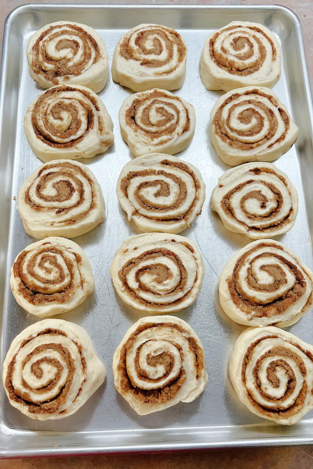 Freshly sliced cinnamon rolls placed onto a baking sheet to raise. 