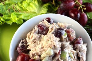 Chicken salad with red grapes and walnuts in a white bowl.