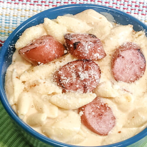 Bowl of creamy mac and cheese topped with kielbasa sausage coins.