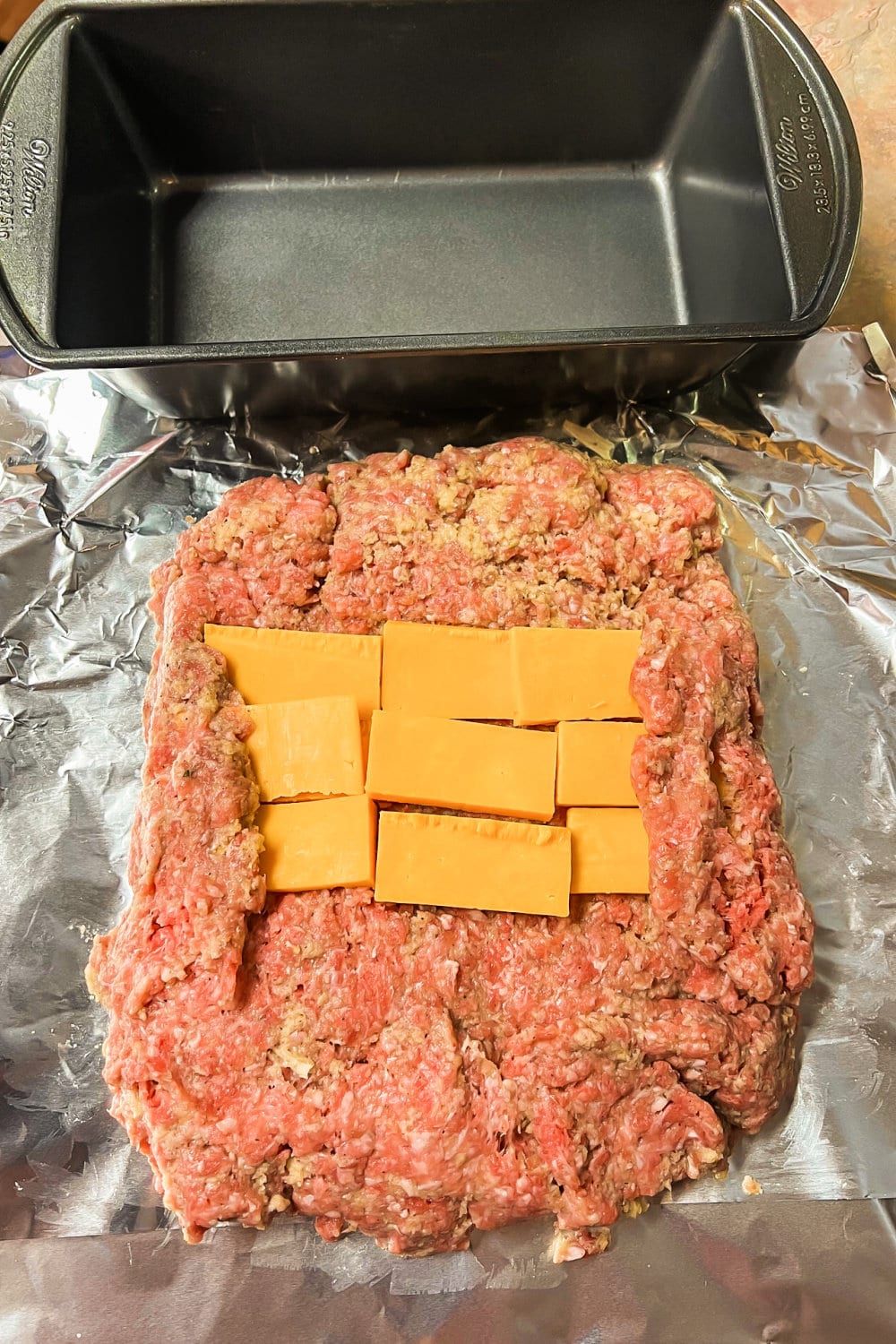 Meatloaf mixture patted out with sliced cheese on top for stuffing.