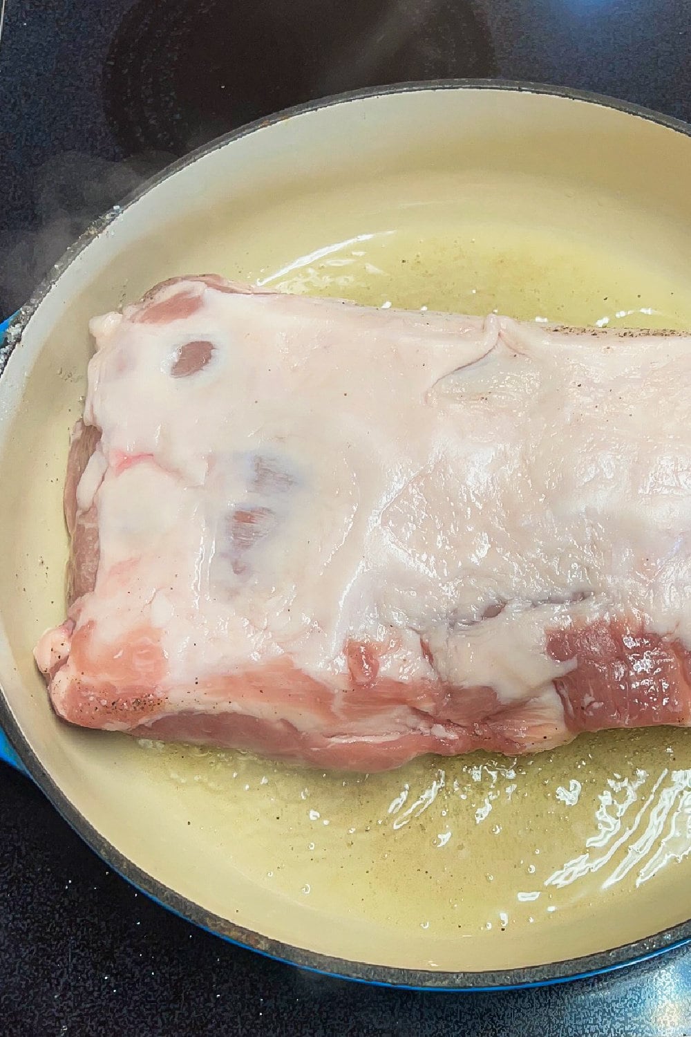 Searing a pork loin in hot oil, fat-side up.
