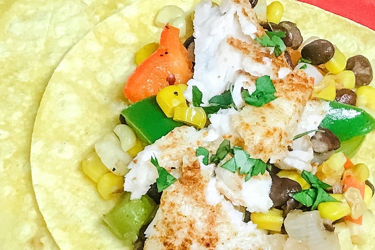 A corn tortilla topped with vegetable hash and crumbled tilapia fish.