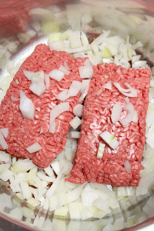 Chunks of ground beef and white onions in a pot. 
