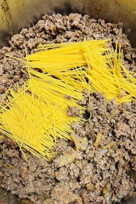 Broken spaghetti pieces added to cooked ground beef. 