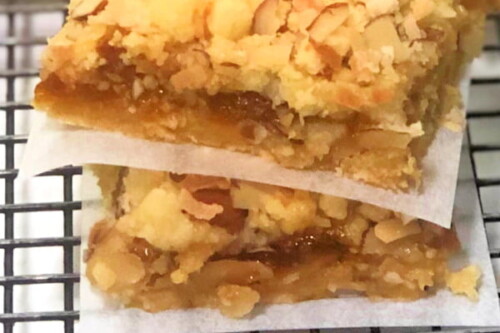 Two apricot almond dessert bars stacked on on top of the other with a square of parchment paper in between, placed on a cooling rack.