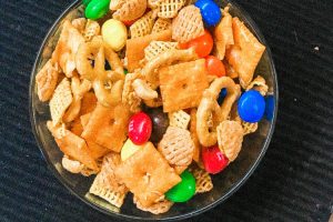 A bowl of party mix with candy.