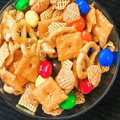 A bowl of party mix with candy.