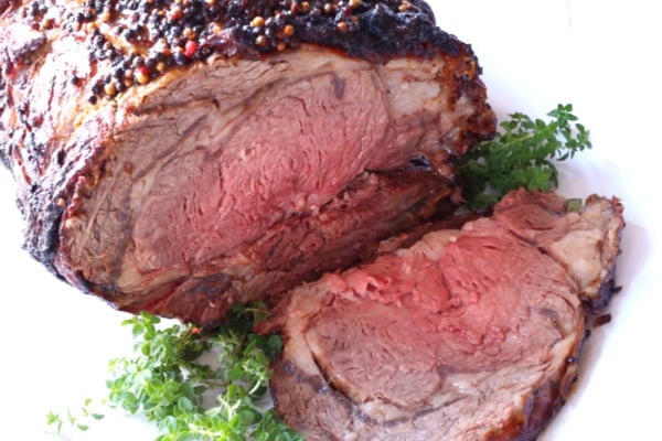 Slice of prime rib resting on a platter beside the standing rib. This picture shows the medium-rare interior of the roast.