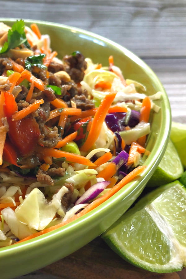 Side view of an Asian beef bowl with vegetable slow and limes. 