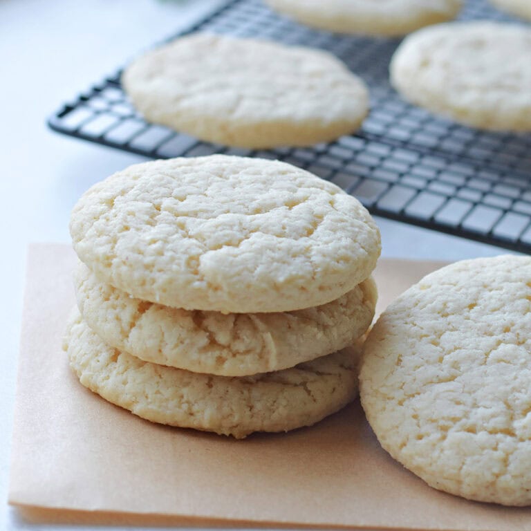 Old Fashioned Sugar Cookies stacked with some on a cooling rack.