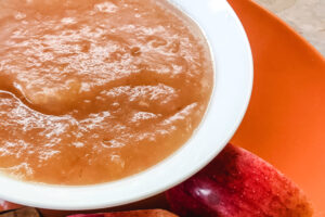 A white bowl of applesauce on an orange plate.