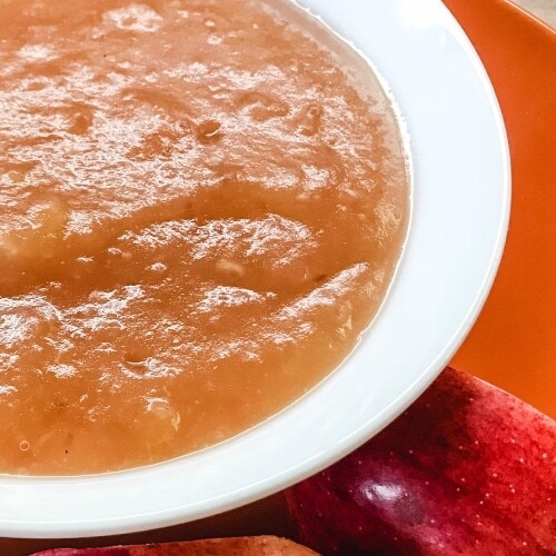 A white bowl of applesauce on an orange plate.