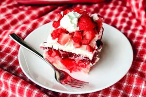 A slice of White Chocolate Strawberry Poke Cake on a plate with a fork.