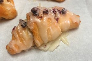 Baked crescent roll dough pastries filled with dried cranberries and toasted walnuts, topped with a powdered sugar glaze.