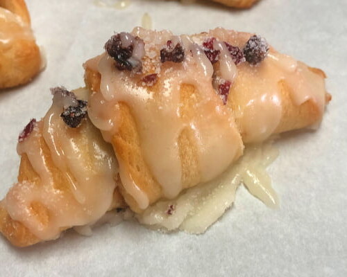 Baked crescent roll dough pastries filled with dried cranberries and toasted walnuts, topped with a powdered sugar glaze.
