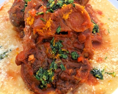 Two pork osso bucco piled on top of each other over a bed of warm parmesan polenta.