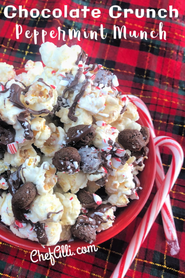 A red bowl full of kettle corn mixture of white chocolate, bite-size chocolate cookies, dark chocolate and crushed peppermint candy canes.