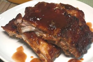white plate with two servings of baby back ribs with bbq sauce