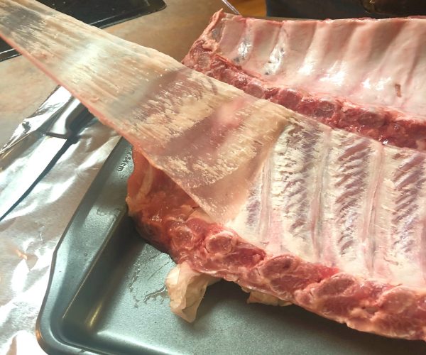 Underside of a rack of baby back ribs as membrane is being pulled back. 