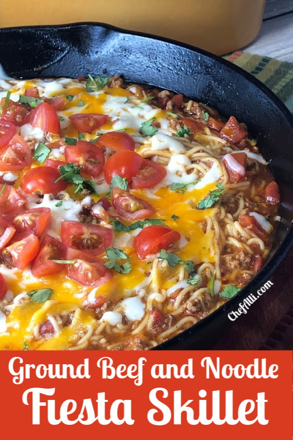 Cast iron skillet full of Fiesta Ground Beef and Noodle Skillet, topped with cheese, tomatoes, and cilantro. 