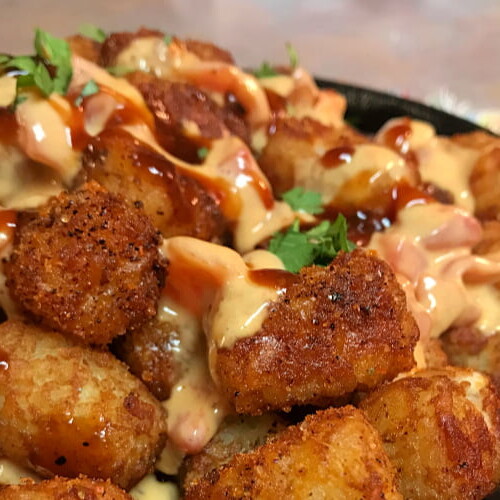 Twisted Mexican Hot Tots layered into a skillet with queso.