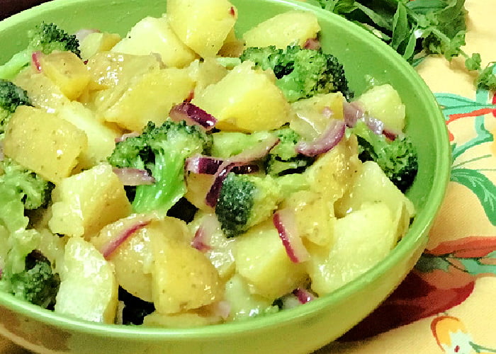 A bowl of potato salad with red onions and broccoli florets.