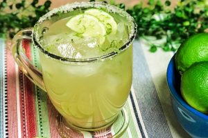 A margarita cocktail with a ice, limes, and a salted rim.