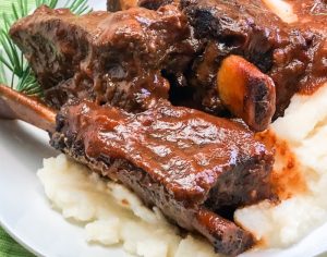 A trio of beef short ribs with sauce on a bed of mashed potatoes.