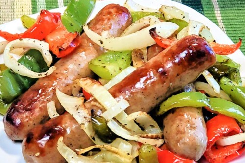 Air Fryer Brats on a bed or peppers and onions sitting on a white plate.
