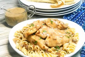 A plate full of noodles topped with chicken tender and gravy.