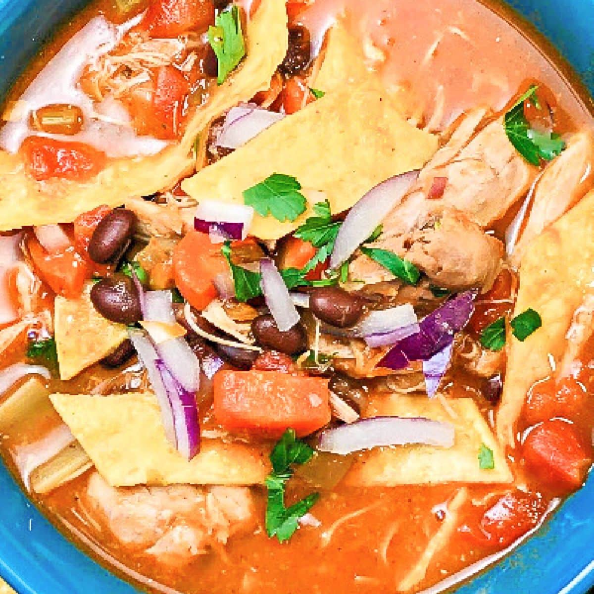 A bowl of chicken tortilla soup that is garnished with chips, onions and tomatoes.