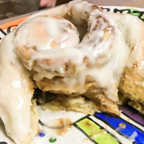 A very large glazed cinnamon roll, partially eaten.