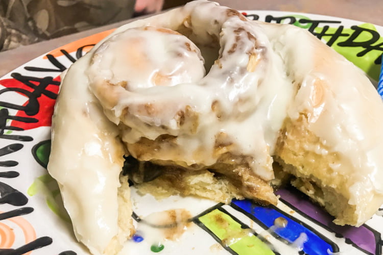 A very large glazed cinnamon roll, partially eaten.