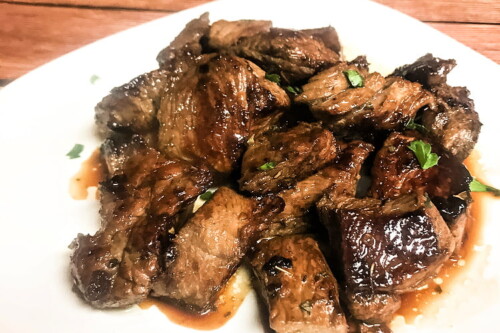 A white plate loaded with marinated steak bites in juices.