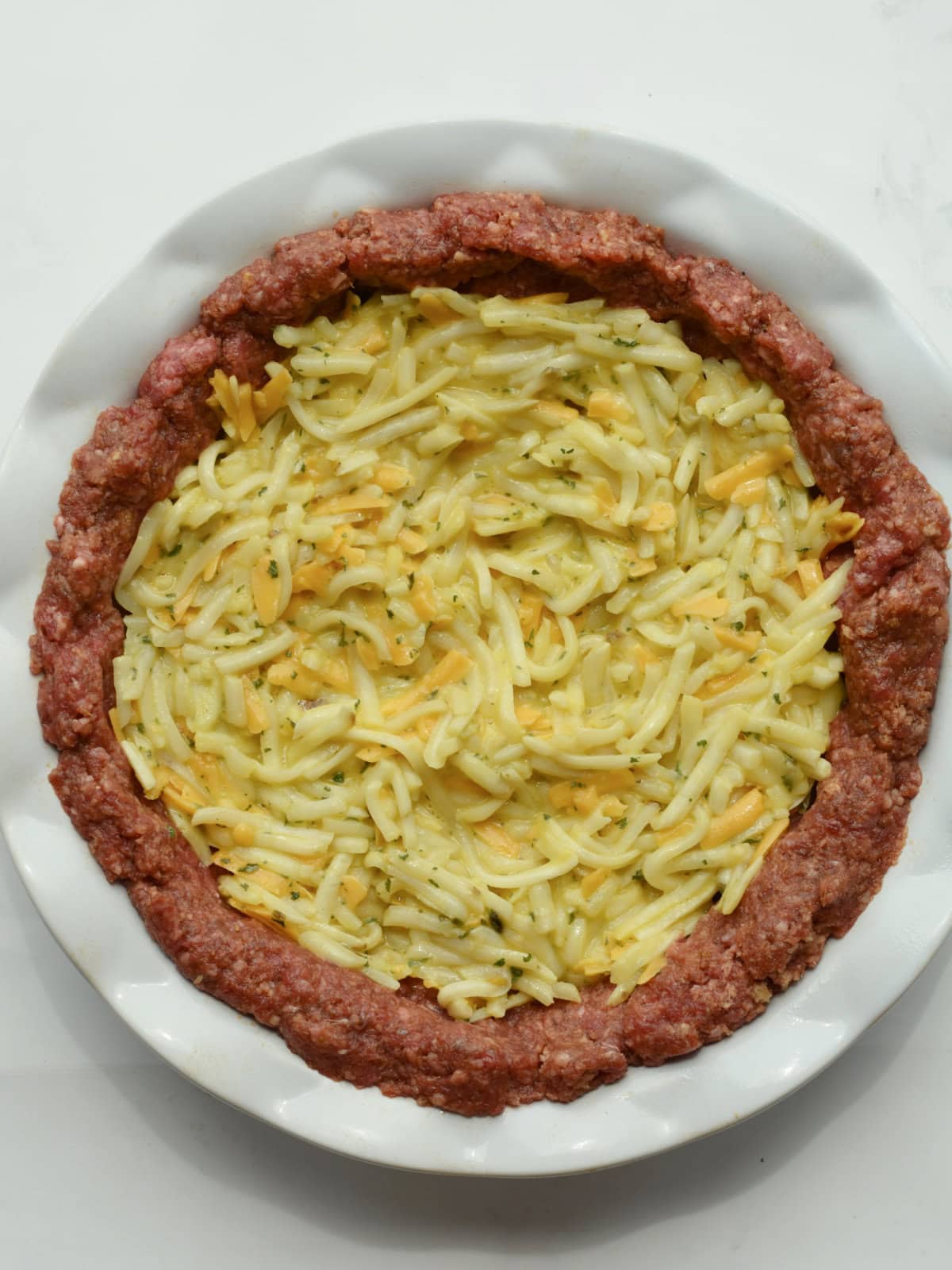Meatloaf-Pie-Raw Raw seasoned ground beef lined with cheesy potatoes in a dish.