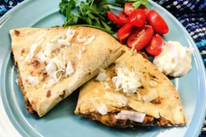 Two quesadilla triangles stacked on a plate with tomatoes and cilantro.