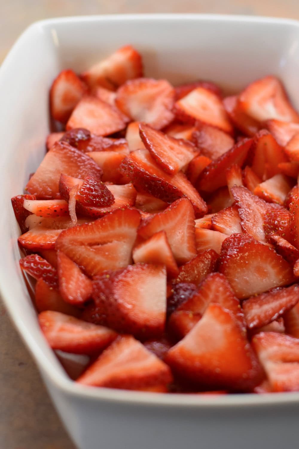 Sliced fresh strawberries placed over the bottom of a white baking dish. 