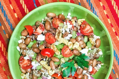 A bright green serving bowl with pinto bean salad and veggies.