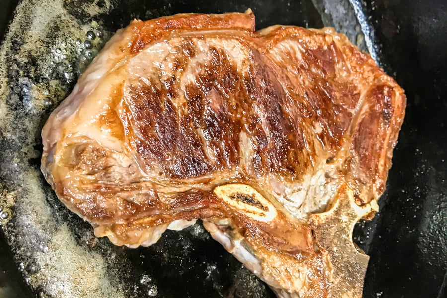 A big, fat, caramelized t-bone steak cooking in a cast iron skillet. 