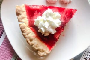 Overhead view of a slice of fresh strawberry pie topped with whipped cream.