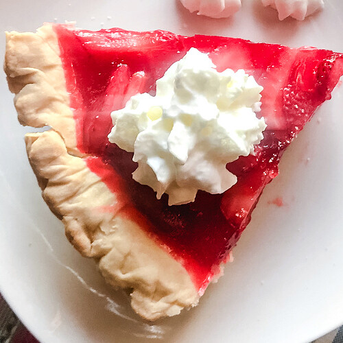 Overhead view of a slice of fresh strawberry pie topped with whipped cream.