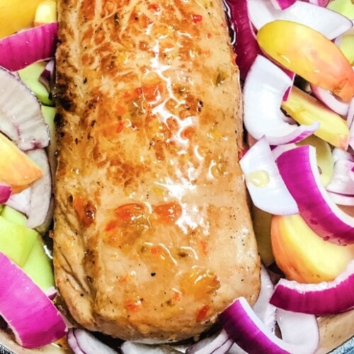 A glazed pepper jelly pork loin nestled in a bed of red onions and sliced apples.
