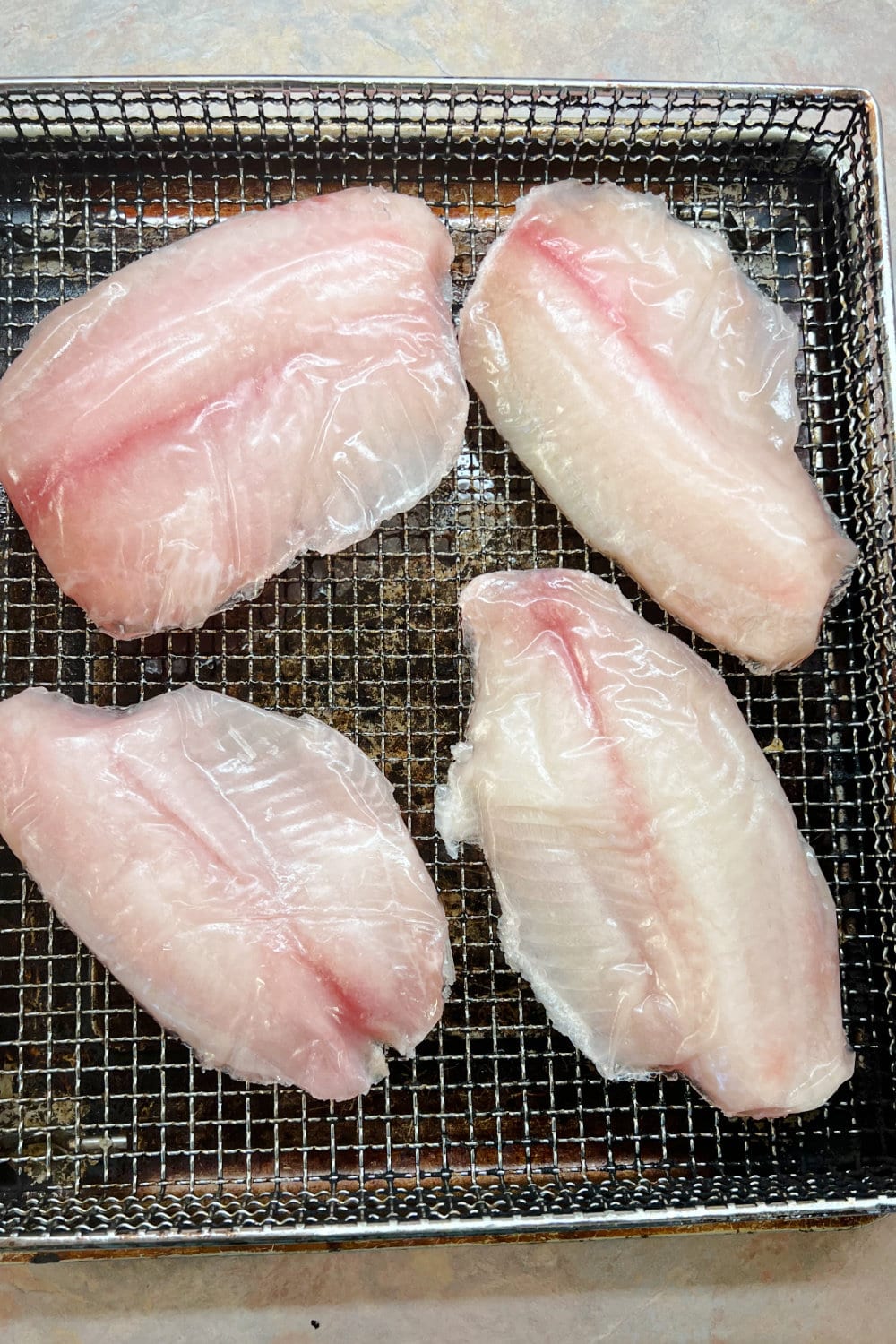 Frozen tilapia fillets placed onto the air fryer rack. 