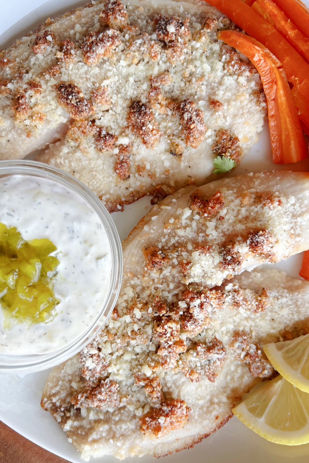 A plate with tilapia fillets, tartar sauce and roasted carrots. 