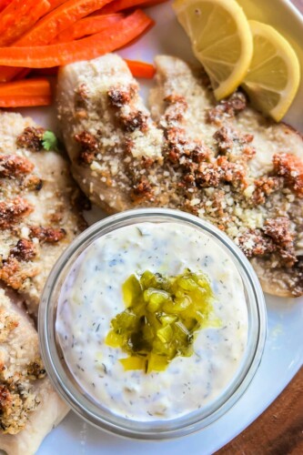 Dill tartar sauce beside fish fillets with parmesan crumbles on top. 